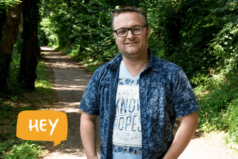 Portretfoto van Michiel in het bos met een oranje spreekwolkje met het woord 'hey' erin in witte letters